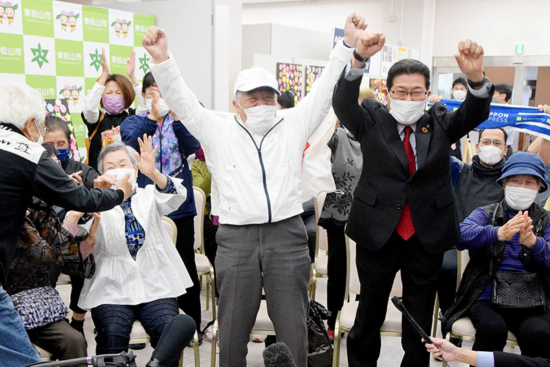 優勝が決まり万歳をして喜ぶ榎田達治さん（中央）、左は妻の和子さん、右は森田光一市長＝埼玉県東松山市総合会館