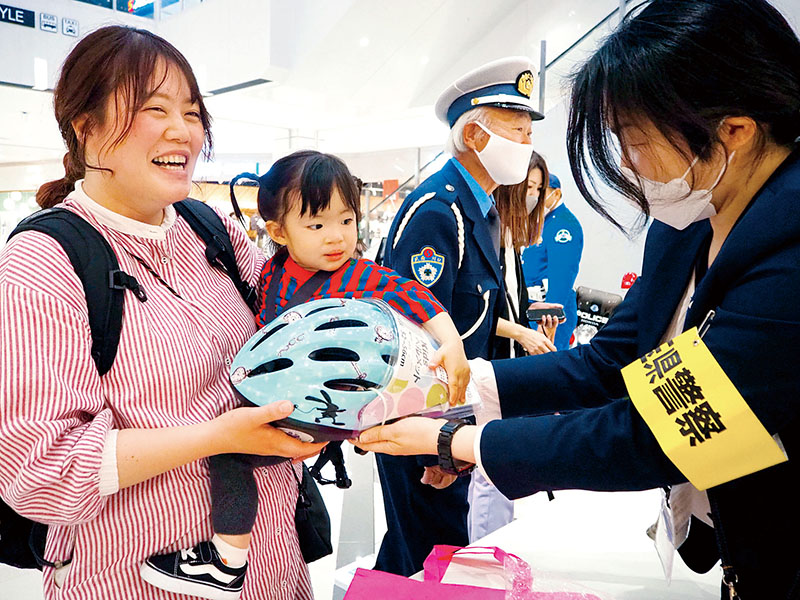 抽選の当選者にヘルメットを手渡す県警職員＝27日、イオンモール川口