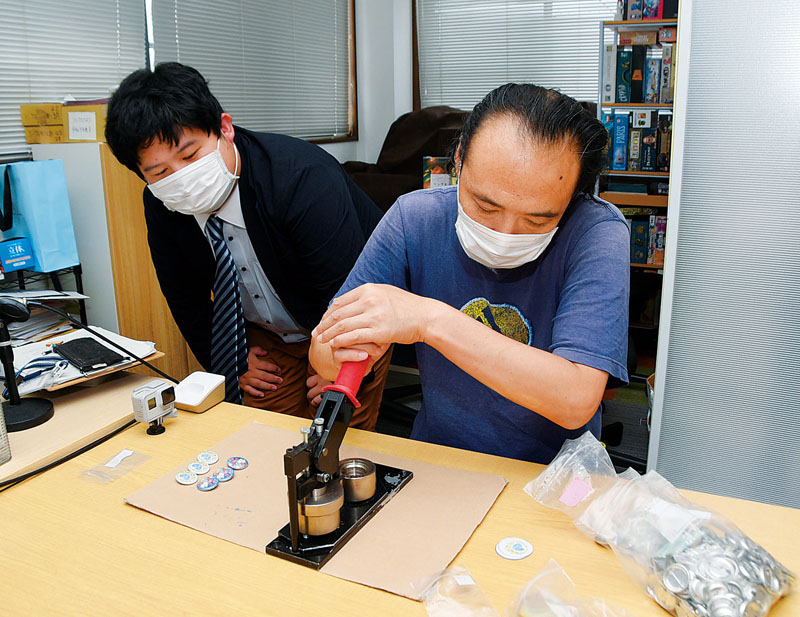 花手水の缶バッジを作る利用者の作業を見守る代表理事の石井浩太さん（左）＝埼玉県川越市砂のリンクス川越事業所