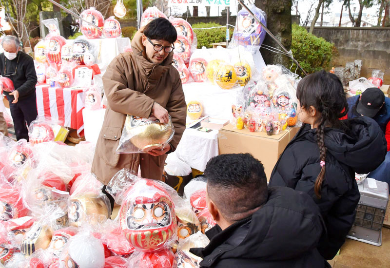 だるまを品定めする参拝客に説明する露店関係者（奥）＝3日、川越市小仙波町の喜多院