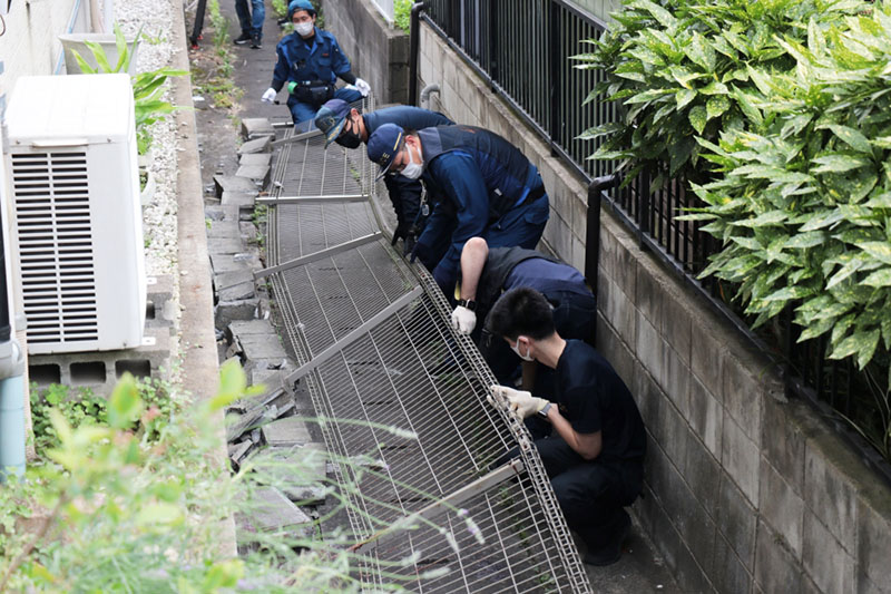 倒れたフェンスを持ち上げる県警の捜査員ら＝13日午後0時半ごろ、越谷市大沢