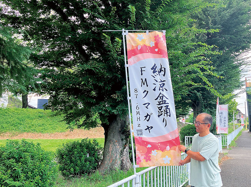 万平公園に並ぶ協賛のぼりと椎名さん。後ろは旧熊谷桜堤＝熊谷市万平町