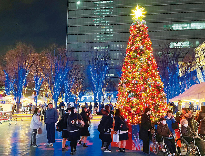 シンボルの赤いツリーの下で撮影するなどクリスマスマーケットを楽しむ人たち