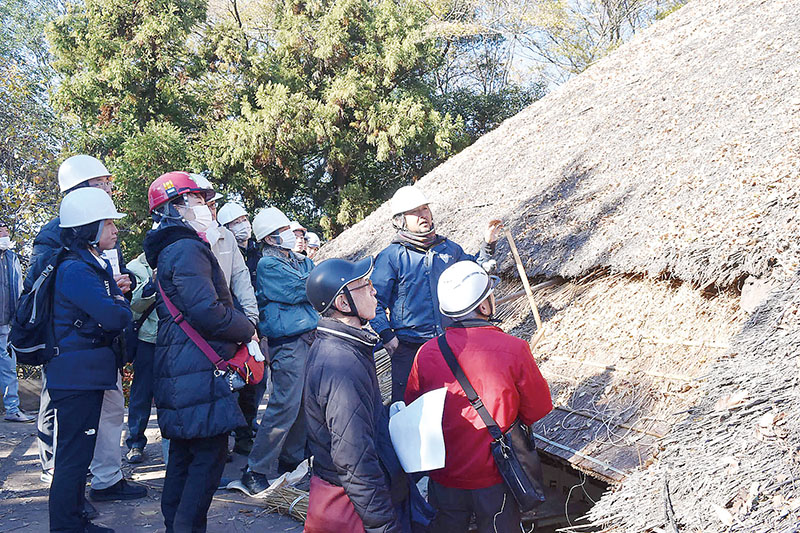 本堂のかやぶき屋根のふき替え工事を見学する関係者たち＝7日午前、熊谷市上中条の常光院