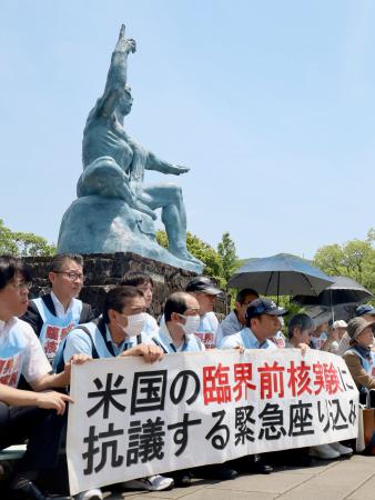 　米国の臨界前核実験に抗議し、平和祈念像の前で座り込む被爆者ら＝２１日午後、長崎市の平和公園