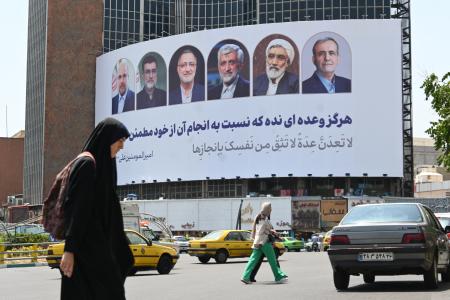 １５日、イランの首都テヘランで全身を覆う黒い衣装を着た女性。後ろには大統領選候補者の看板が設置されていた（共同）