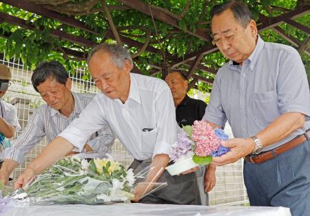 　松本サリン事件から３０年となるのを前に、犠牲者が出た寮跡地に設置した献花台に花を供える田町町会の吉見隆男会長（中央）ら＝２６日午前、長野県松本市