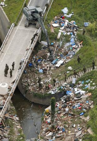 災害ごみに覆われた用水路付近で作業をする自衛隊員ら＝２０１８年７月２７日午前、岡山県倉敷市真備町地区