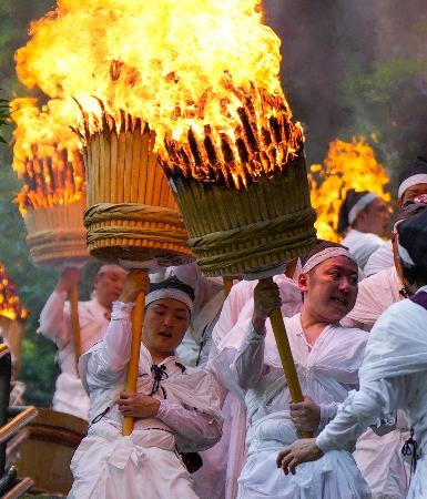 熊野那智大社の例大祭「那智の扇祭り」で、燃えさかる大たいまつを担ぎ練り歩く白装束の氏子ら＝１４日午後、和歌山県那智勝浦町