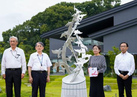 　京都府宇治市の公園に設置された「志を☆（繋の車のタテ棒が山）ぐ碑」。左から２人目は京都アニメーションの八田英明社長＝１４日午前