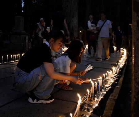 　高野山・奥の院で行われた「ろうそくまつり」で火をともす女性＝１３日夜、和歌山県高野町