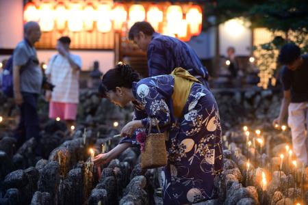 化野念仏寺で始まった「千灯供養」で、石仏にろうそくをともす参拝者＝２４日夕、京都市