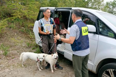 北海道駒ケ岳で登山者（左）に噴火情報に関するパンフレットを配布する協議会の関係者＝２６日午前