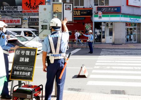 持ち運び可能な発電機（左下）から給電し、信号を作動させる警察官＝６日午前、札幌市