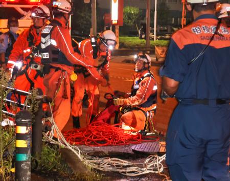 作業員２人が流された現場周辺で、下水道管を調べる消防隊員＝１９日夜、相模原市