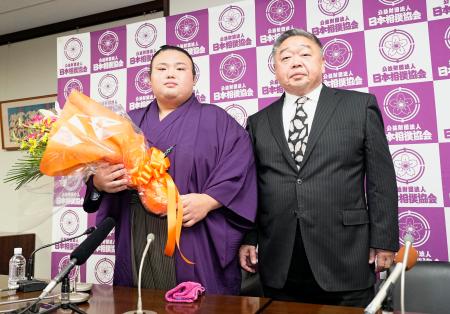 　現役引退の記者会見で、花束を手にする元大関貴景勝。右は常盤山親方＝２１日、東京・両国国技館