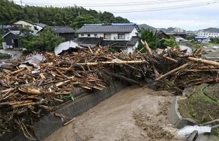 豪雨で増水した石川県輪島市の塚田川沿いで、家屋の前に積み重なった無数の流木＝２２日午前１１時１９分