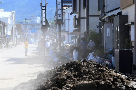 泥が乾燥し砂ぼこりが舞う中、片付けに追われる人たち＝２５日午前、石川県輪島市