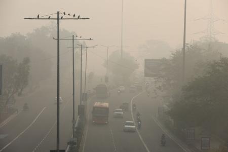 　大気汚染で煙に覆われた道路を進む車両＝２０２３年１１月、インドの首都ニューデリー（ロイター＝共同）