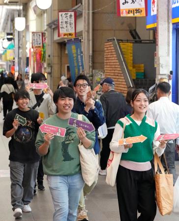 投票を呼びかける矢印を手に商店街を歩く学生たち＝２１日、北九州市