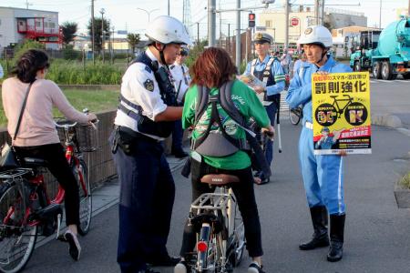 自転車走行中の携帯電話使用などに罰則を新設した改正道交法の施行を前に、新たなルールを周知する埼玉県警の警察官ら＝３０日午後、埼玉県草加市