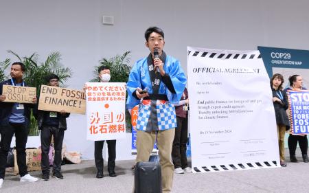 ＣＯＰ２９の会場で化石燃料への公的支援停止を訴える高田陽平さん（手前）ら＝１８日、アゼルバイジャン・バクー（共同）