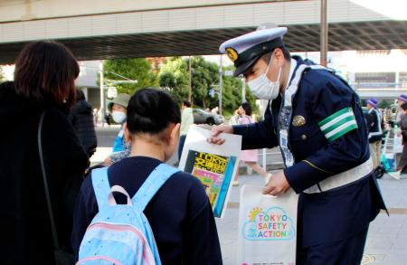 歩行者に反射材を配り、夕暮れ時や夜間の外出時の着用を呼びかける警視庁の警察官＝１日午後、東京都渋谷区