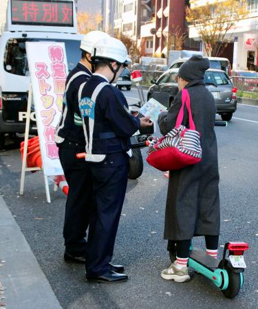 電動キックボードの利用者にチラシを配る警視庁の警察官＝６日午後、東京都港区